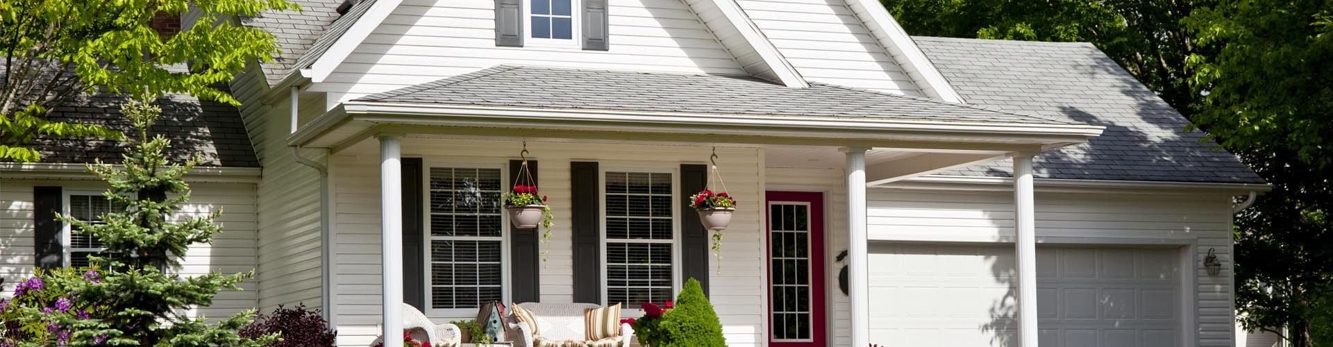 A white house with new siding, black shutters, and a red front door.