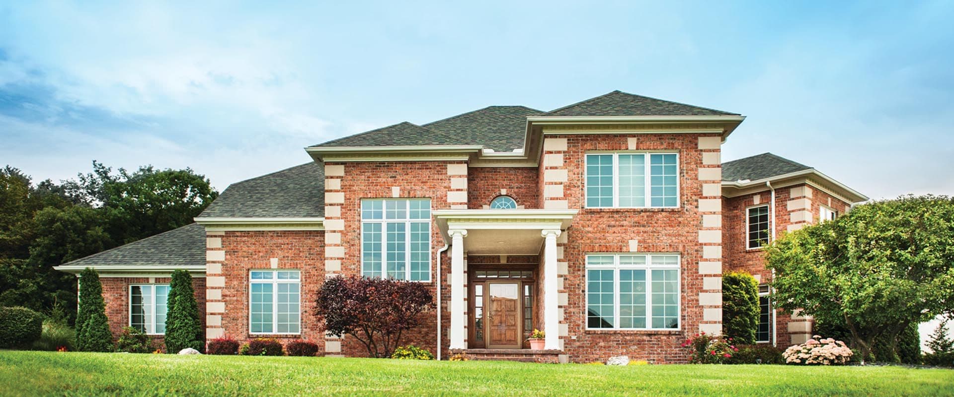 A large red brick house with brown entry door and new windows.