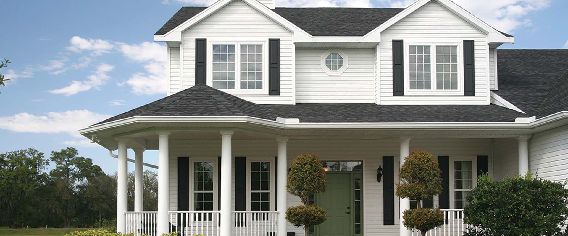 A white house with new siding, a porch, and a green front door.